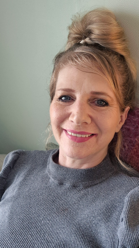 Kate - a blonde woman wearing a grey top, is smiling at the camera