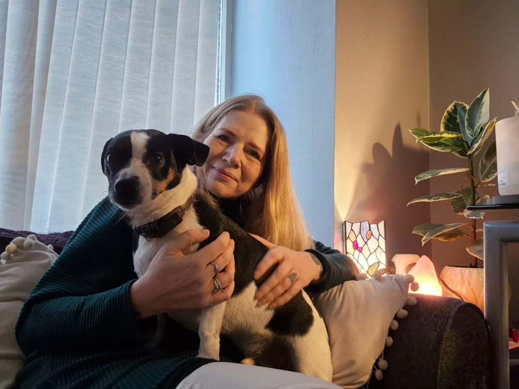 Kate, a blonde woman, is sitting on her sofa, with her small black and white Jack Russell terrier, on her knee